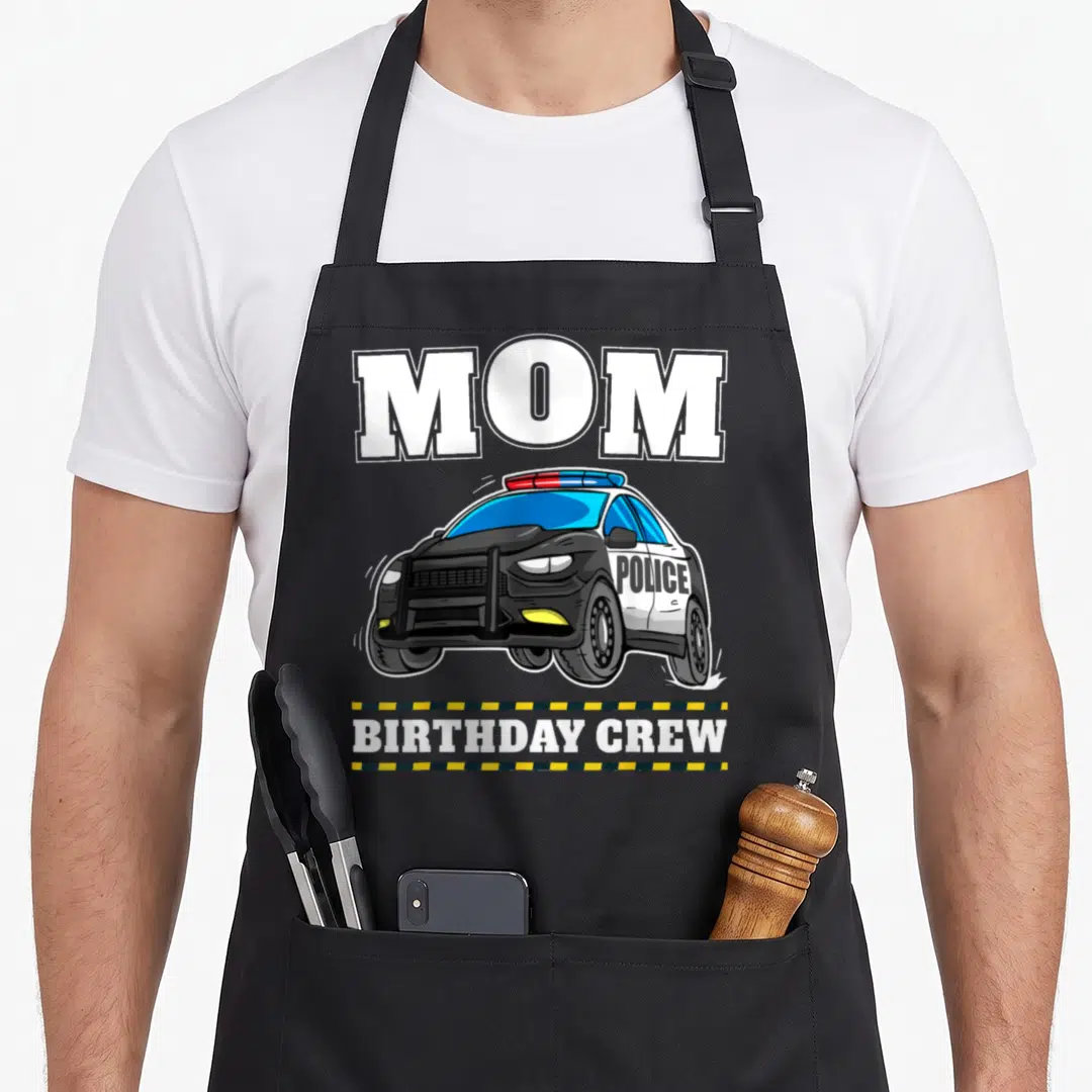 Police crew aprons - MOM BIRTHDAY CREW text surrounding a cartoon police car with yellow and black caution tape border — shown on a black cotton canvas apron against a white background