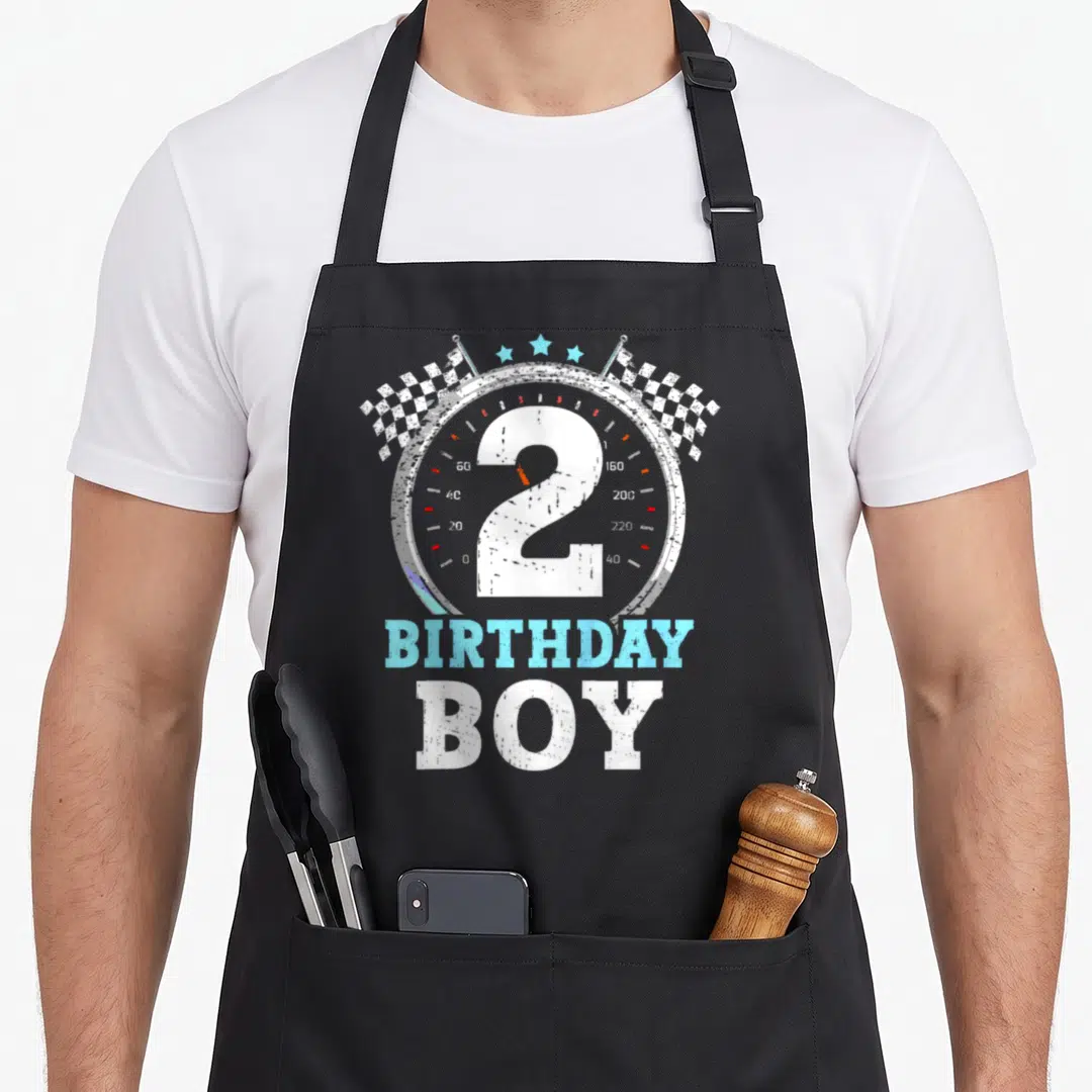 Flag 2nd apron - Speedometer with number 2, checkered flags, stars, and BIRTHDAY BOY text in distressed style — shown on a black cotton canvas apron against a white background