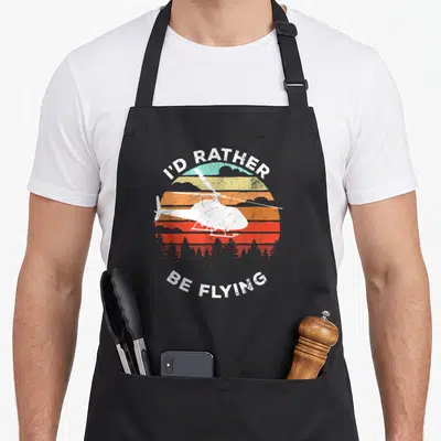 Helicopter flying apron - White helicopter silhouette over retro striped sun with arched text I'D RATHER BE FLYING — shown on a black cotton canvas apron against a white background