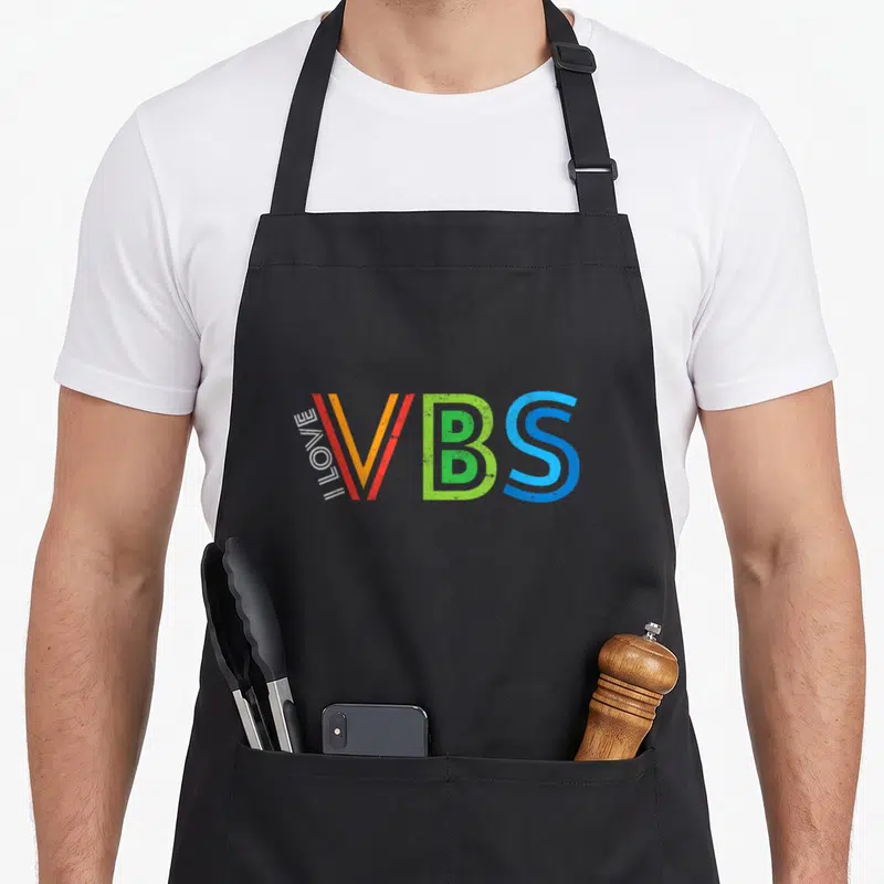 School church aprons - I LOVE VBS typography in orange, green, blue, and white vertical layout — shown on a black cotton canvas apron against a white background