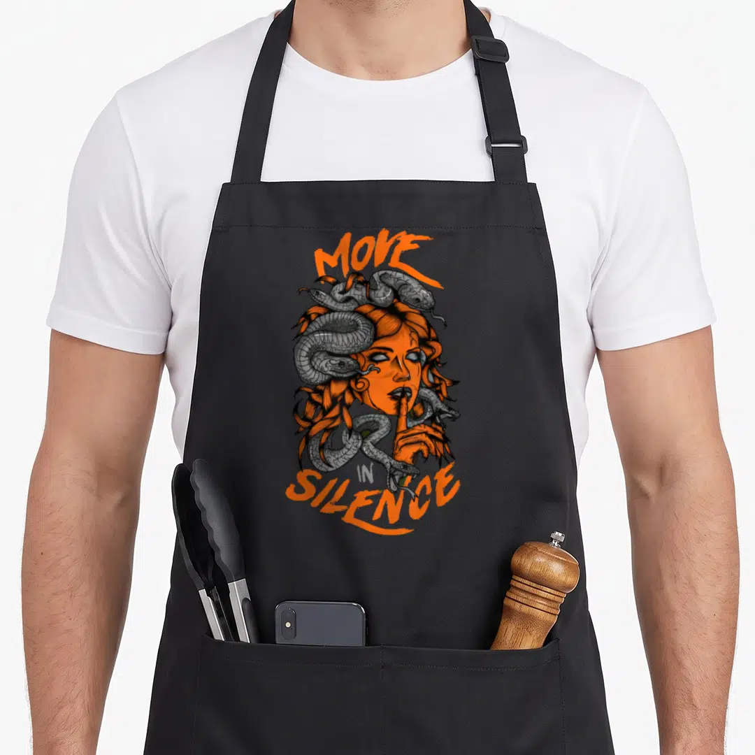 Army novelty apron - Orange and grey Medusa head with snakes and finger to lips flanked by MOVE and SILENCE text — shown on a black cotton canvas apron against a white background