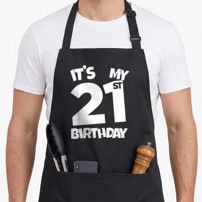 21st twenty birthday apron - White stacked text reading IT'S MY 21ST BIRTHDAY with large central number 21 — shown on a black cotton canvas apron against a white background