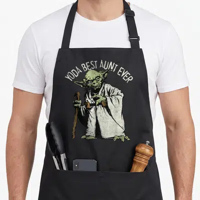 Aunt yoda apron - Yoda Best Aunt Ever arched text above green character holding brown cane — shown on a black cotton canvas apron against a white background