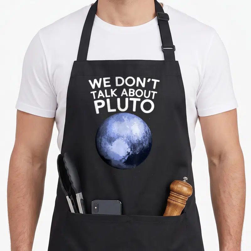 Talk astronomy apron - White text We Don't Talk About Pluto above a realistic blue sphere of the dwarf planet — shown on a black cotton canvas apron against a white background