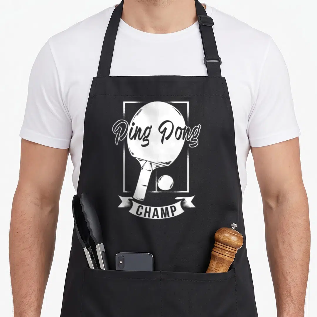 Pong champ table apron - White ping pong paddle and ball in a frame with CHAMP banner text — shown on a black cotton canvas apron against a white background