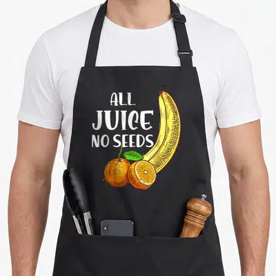 Vasectomy seed juice apron - Cartoon banana and orange with All Juice No Seeds text — shown on a black cotton canvas apron against a white background