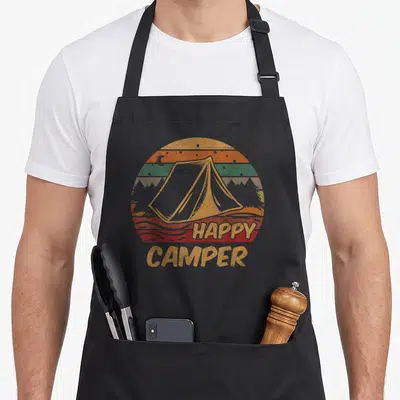 Campsite happy camper apron - Retro tent centered in a striped sunset circle with moon and trees above HAPPY CAMPER text — shown on a black cotton canvas apron against a white background