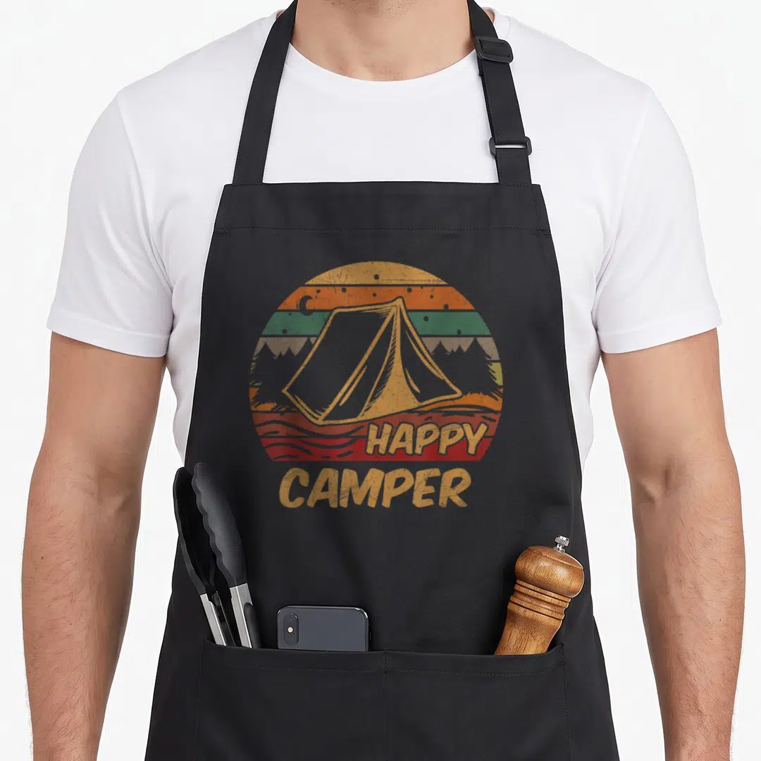 Campsite happy camper apron - Retro tent centered in a striped sunset circle with moon and trees above HAPPY CAMPER text — shown on a black cotton canvas apron against a white background