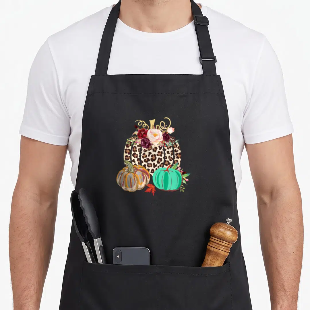 Cheetah thanksgiving apron - Leopard print pumpkin with pink flowers and two smaller orange and teal pumpkins — shown on a black cotton canvas apron against a white background