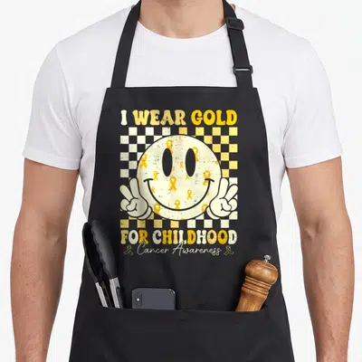 Childhood ribbon apron - Distressed smiley face with gold ribbons and peace hands on yellow checkerboard background — shown on a black cotton canvas apron against a white background