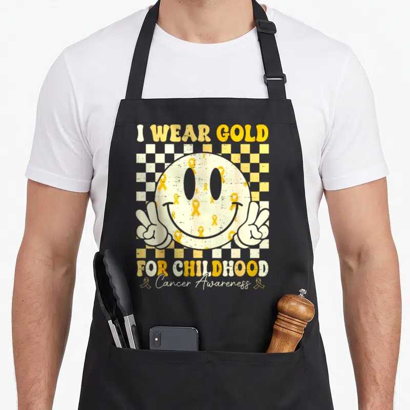 Childhood ribbon apron - Distressed smiley face with gold ribbons and peace hands on yellow checkerboard background — shown on a black cotton canvas apron against a white background