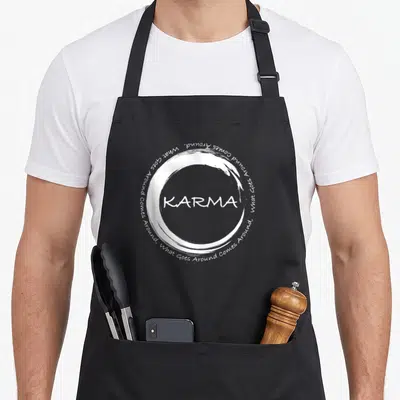 Karma circle time apron - White brush circle with centered KARMA text and surrounding What Goes Around Comes Around — shown on a black cotton canvas apron against a white background