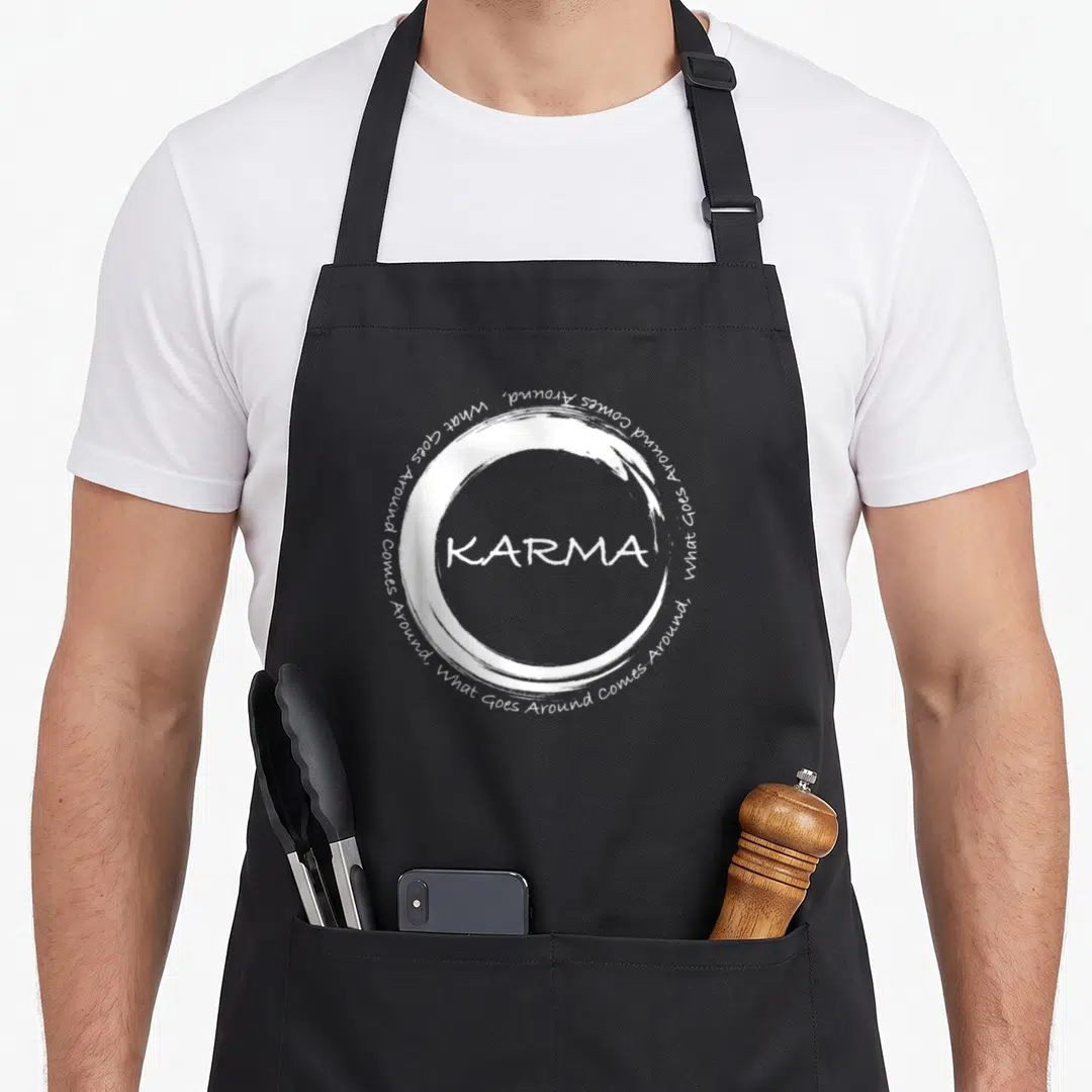 Karma circle time apron - White brush circle with centered KARMA text and surrounding What Goes Around Comes Around — shown on a black cotton canvas apron against a white background