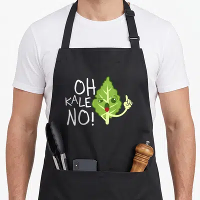Veggie vegan apron - Oh Kale No text beside a pointing cartoon green kale leaf with a face — shown on a black cotton canvas apron against a white background