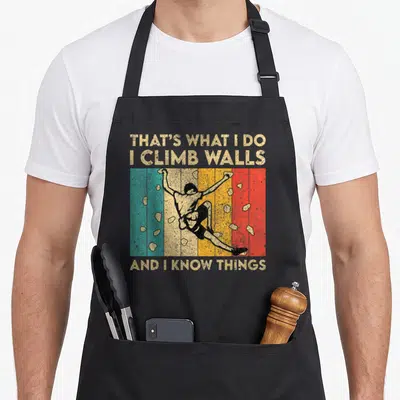 Climb bouldering apron - Retro climber on teal, beige, yellow, orange, and red stripes with scattered holds — shown on a black cotton canvas apron against a white background