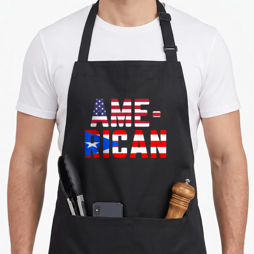Boricua rican apron - Stacked AME- RICAN text filled with US and Puerto Rico flag patterns in red white blue — shown on a black cotton canvas apron against a white background