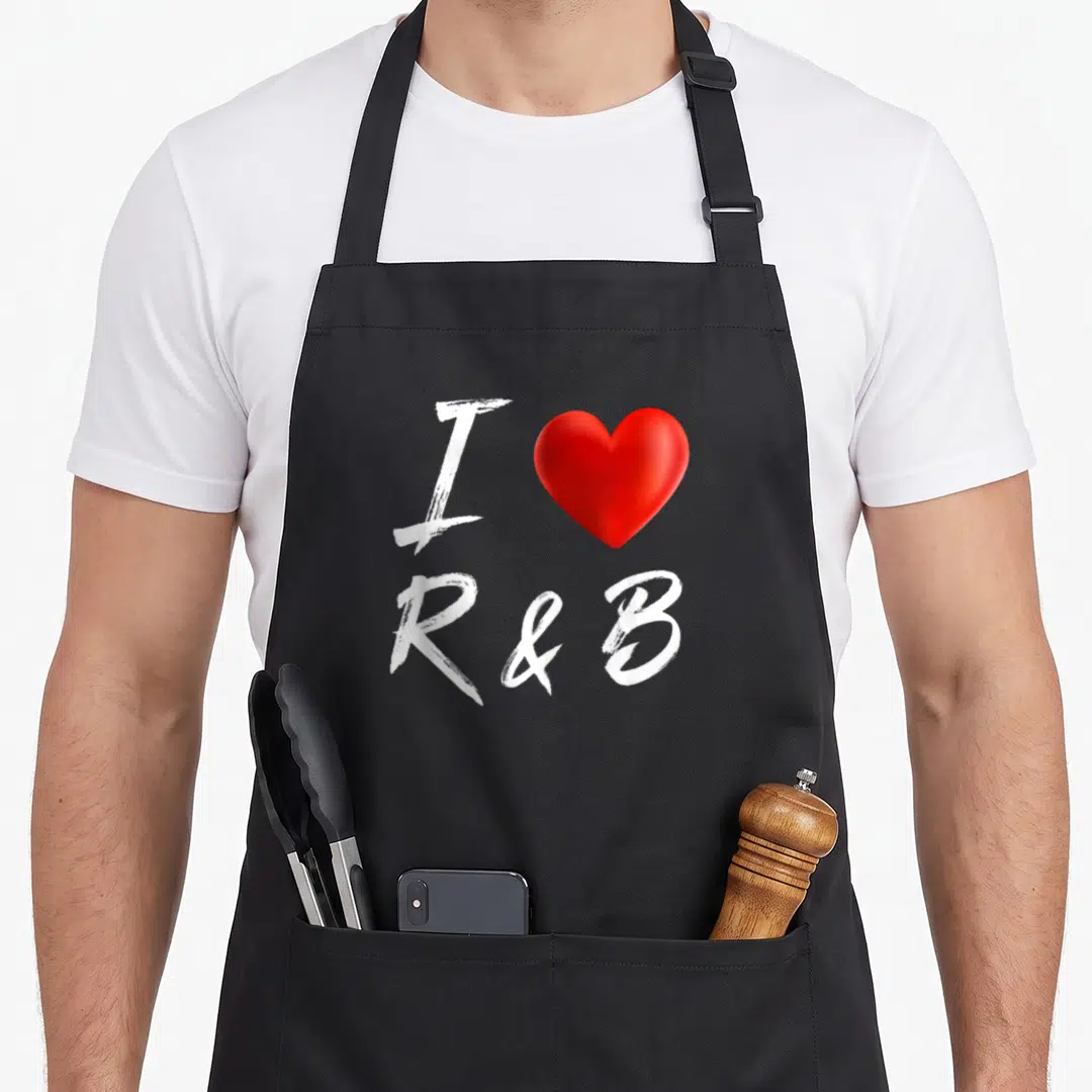 Funny music r aprons - White brush stroke text I R&B with a red heart symbol centered on the fabric — shown on a black cotton canvas apron against a white background