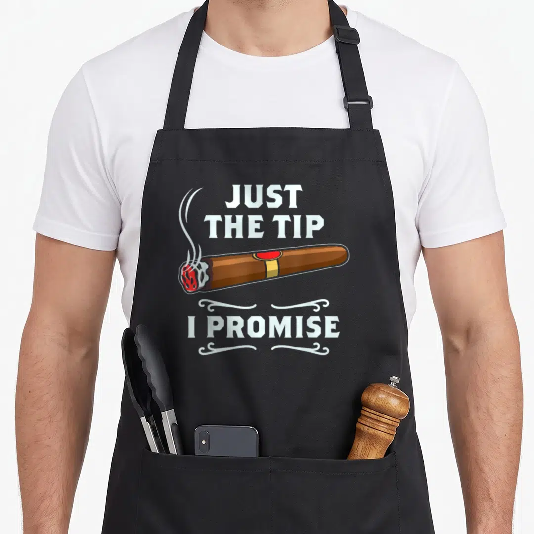 Tip smoking apron - Cartoon brown cigar with red ash and white text JUST THE TIP I PROMISE with swirls — shown on a black cotton canvas apron against a white background