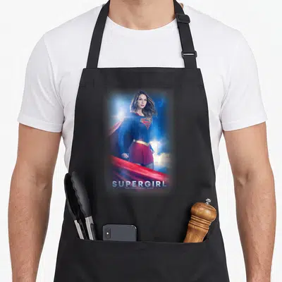 Supergirl thriller apron - Photo of Supergirl in blue and red suit with title text below on a black apron — shown on a black cotton canvas apron against a white background