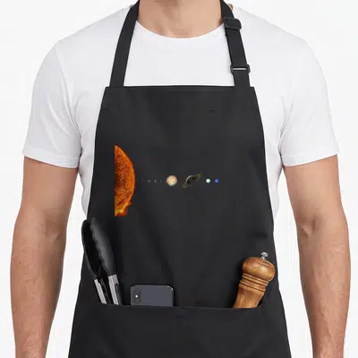 Solar system science apron - Realistic orange sun and horizontal row of blue and beige planets on black background — shown on a black cotton canvas apron against a white background