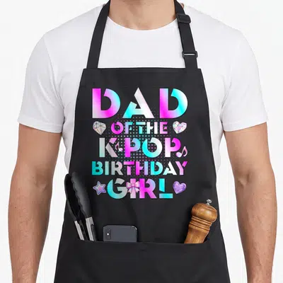 Pop birthday korean apron - DAD OF THE KPOP BIRTHDAY GIRL text in pink cyan purple with diamond star bow heart icons — shown on a black cotton canvas apron against a white background
