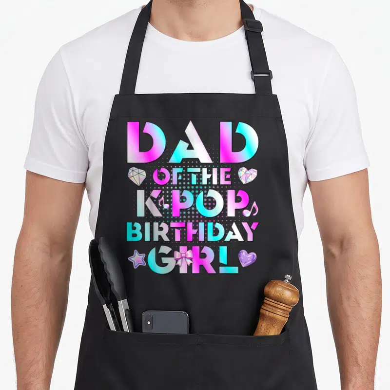 Pop birthday korean apron - DAD OF THE KPOP BIRTHDAY GIRL text in pink cyan purple with diamond star bow heart icons — shown on a black cotton canvas apron against a white background