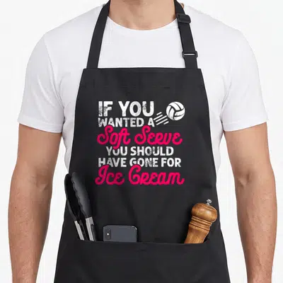 Volleyball practice apron - Stacked white and pink text reading soft serve ice cream with a motion volleyball graphic — shown on a black cotton canvas apron against a white background