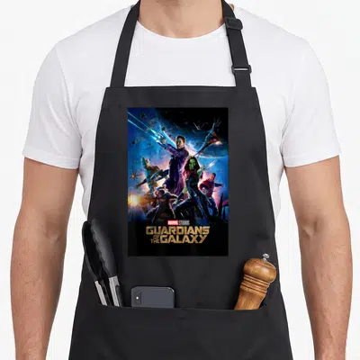 Studio galaxies apron - Guardians of the Galaxy photo print with stacked gold title text and space background — shown on a black cotton canvas apron against a white background