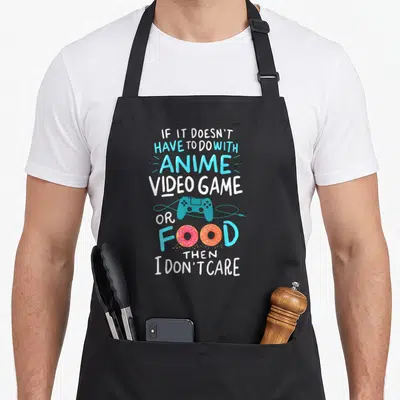 Food video game apron - Stacked text with teal controller and two pink and orange donuts replacing letters in white — shown on a black cotton canvas apron against a white background