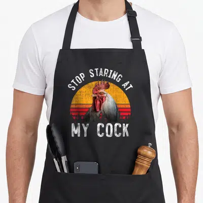Chicken rooster apron - Retro rooster head in front of orange and red striped sun with white text — shown on a black cotton canvas apron against a white background