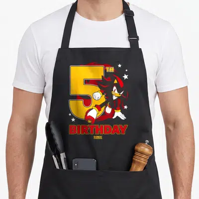 Shadow birthday apron - Shadow the Hedgehog illustration next to yellow number 5 with red flames and BIRTHDAY text — shown on a black cotton canvas apron against a white background