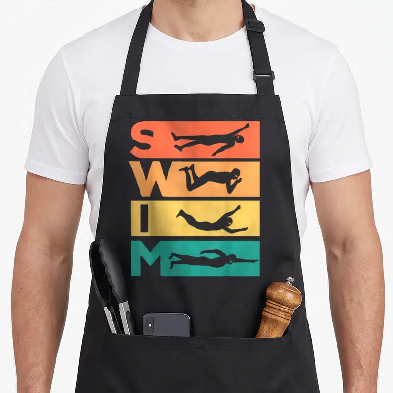 Funny swimmer i love swimming apron - Vertical SWIM text with grey swimmer silhouettes on orange yellow and teal blocks — shown on a black cotton canvas apron against a white background