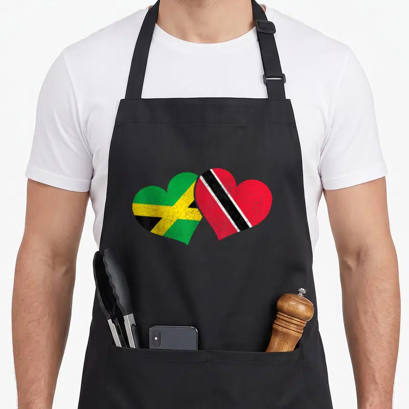 Jamaica trinidad and tobago apron - Two overlapping hearts with Jamaican and Trinidad Tobago flag patterns in green — shown on a black cotton canvas apron against a white background