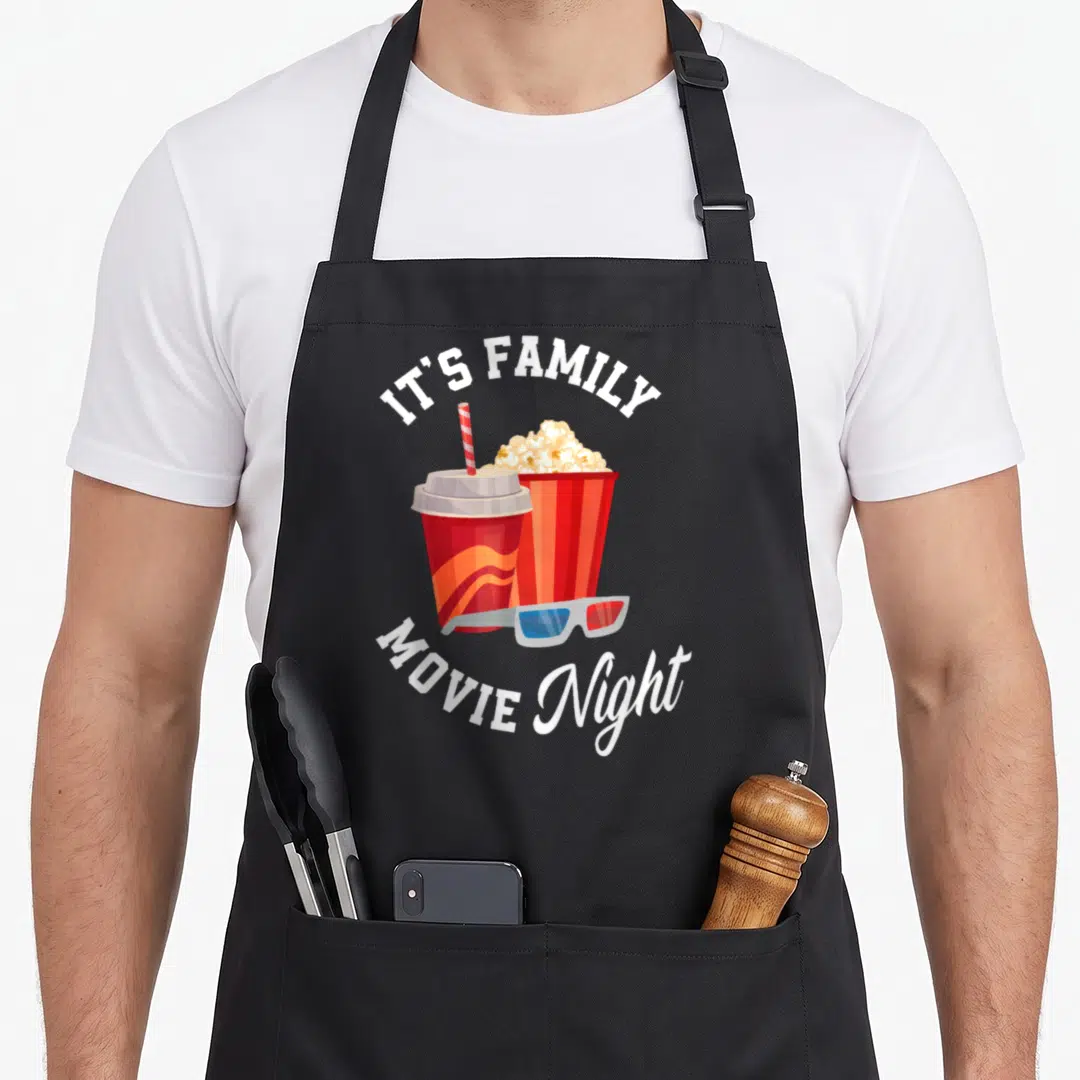 Cinema family aprons - Cartoon soda, popcorn, and 3D glasses framed by white IT'S FAMILY MOVIE Night text — shown on a black cotton canvas apron against a white background