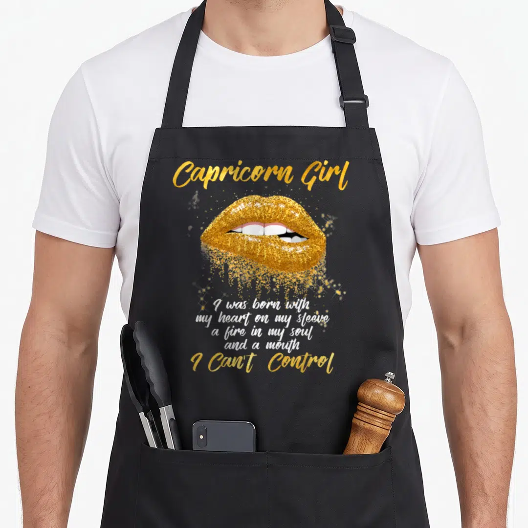 Funny capricorn birthday apron - Gold glitter lips with Capricorn Girl text and white quote on grey background — shown on a black cotton canvas apron against a white background