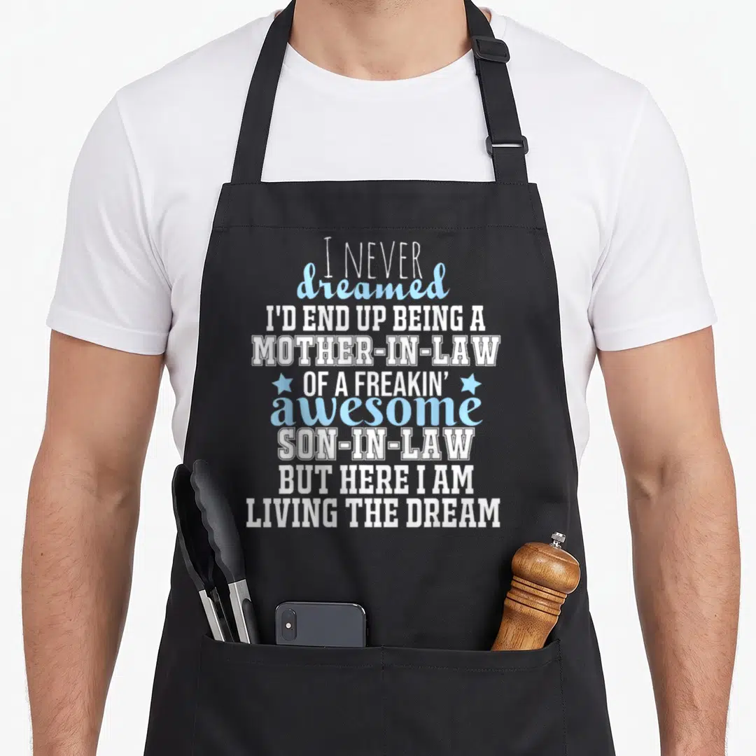 End mother's apron - Stacked white and blue text reading I Never Dreamed I'd End Up Being A Mother-In-Law with two stars — shown on a black cotton canvas apron against a white background