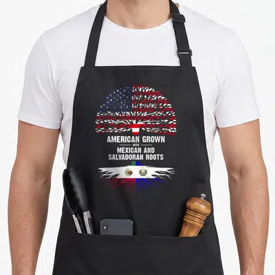 Grown salvadoran apron - Tree with red white blue leaves and roots showing Mexican and Salvadoran flags alongside — shown on a black cotton canvas apron against a white background