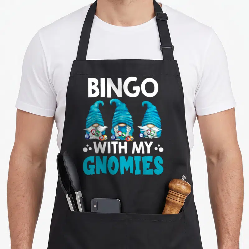 Gnomy bingo apron - Three cyan gnomes holding bingo balls with BINGO WITH MY GNOMIES text — shown on a black cotton canvas apron against a white background