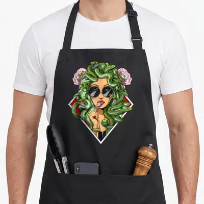 Medusa greek aprons - Medusa head with green snakes, sunglasses, pink lollipop, and roses in red white diamond frame — shown on a black cotton canvas apron against a white background