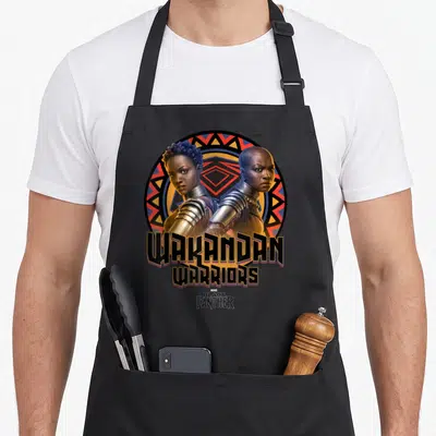 Movie panther apron - Two warriors back-to-back in a circle with WAKANDAN WARRIORS text — shown on a black cotton canvas apron against a white background