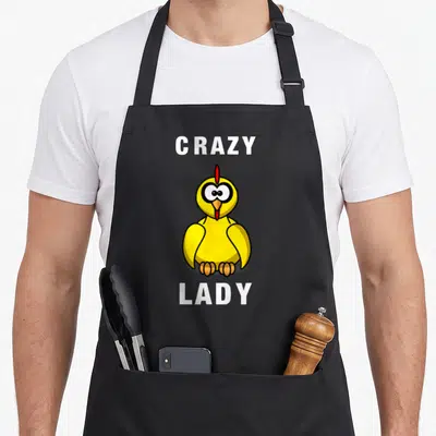 Animal chicken with apron - Cartoon yellow chicken between white Crazy and Lady text — shown on a black cotton canvas apron against a white background