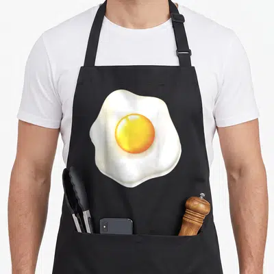 Costume egg apron - Realistic fried egg print with yellow yolk and white edges on black fabric — shown on a black cotton canvas apron against a white background