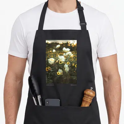 Nathan sunflower apron - Rectangular photo of yellow sunflowers and white blooms with NATHAN KAWANISHI text below — shown on a black cotton canvas apron against a white background