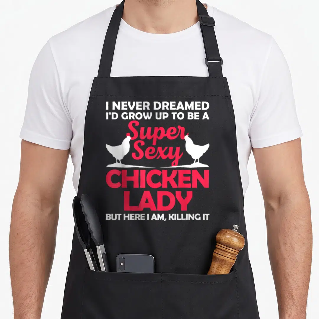 Retro farmer chicken with apron - Red and white stacked text reading Super Sexy Chicken Lady flanked by two white — shown on a black cotton canvas apron against a white background