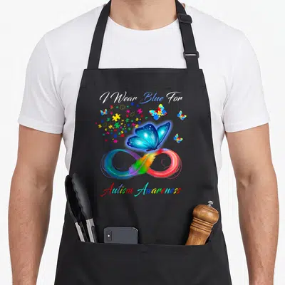 Blue anxiety awareness apron - I Wear Blue For Autism Awareness text with blue butterfly on rainbow infinity symbol — shown on a black cotton canvas apron against a white background