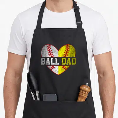 Ball father day apron - Split heart graphic with white baseball and yellow softball halves and distressed BALL DAD text — shown on a black cotton canvas apron against a white background