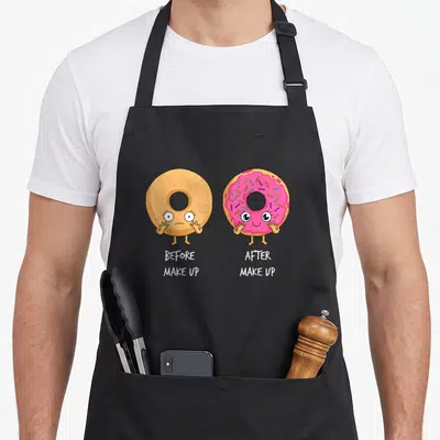 Funny doughnut donut apron - Two cartoon donuts side by side, one plain tan and one pink frosted with sprinkles — shown on a black cotton canvas apron against a white background