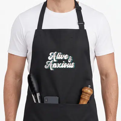 Alive anxiety anxious apron - White script text reading Alive & Anxious with colorful striped 3D shadows — shown on a black cotton canvas apron against a white background