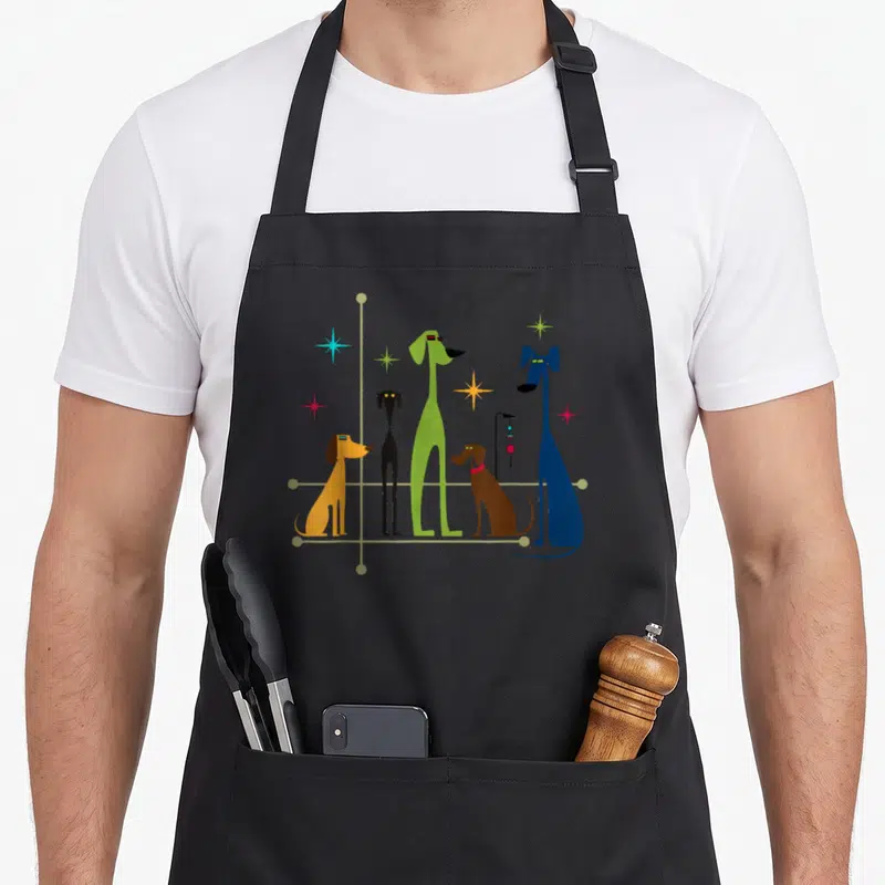 Mid century dog modern apron - Five stylized long-legged dogs in yellow, black, green, brown, and blue surrounded — shown on a black cotton canvas apron against a white background