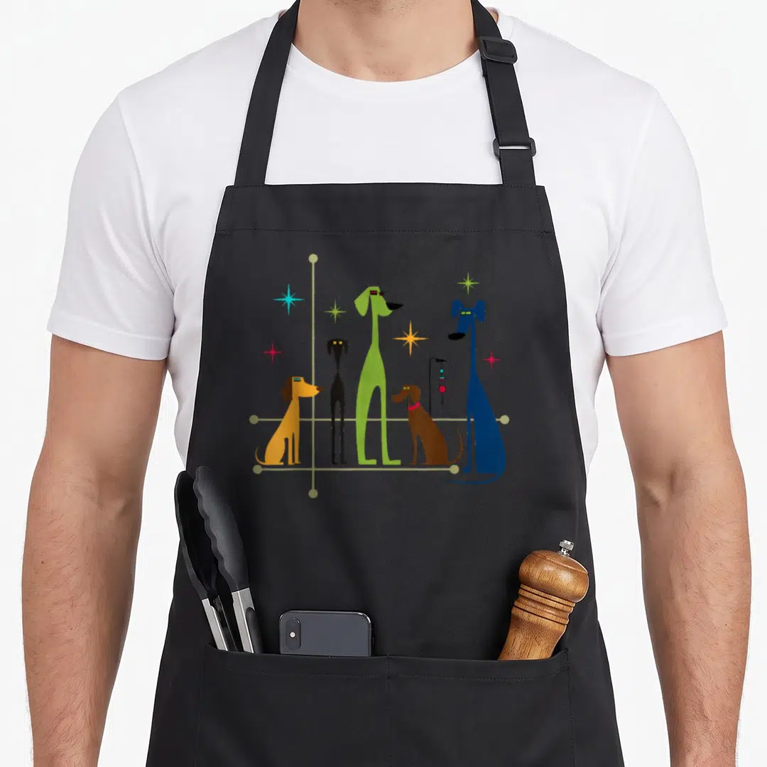 Mid century dog modern apron - Five stylized long-legged dogs in yellow, black, green, brown, and blue surrounded — shown on a black cotton canvas apron against a white background